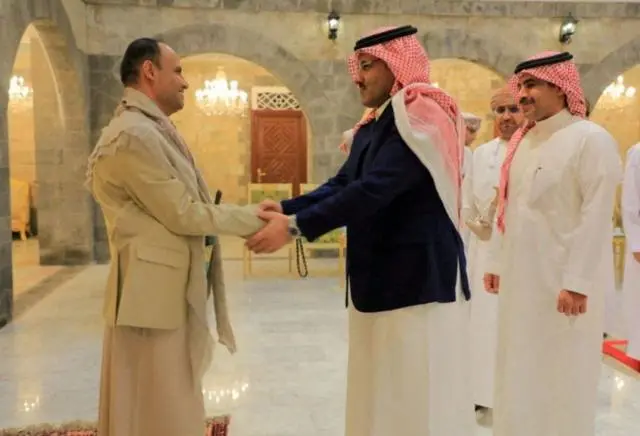 المشاط مصافحاً آل جابر وكلاهما يرتدي اللباس التقليدي (ثوب وعليه سترة بدلة).