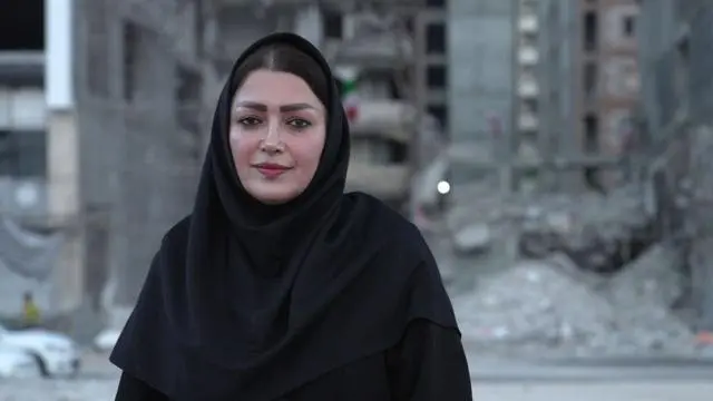 امرأة تنظر مباشرة إلى الكاميرا، مرتدية ملابس سوداء وحجاباً.