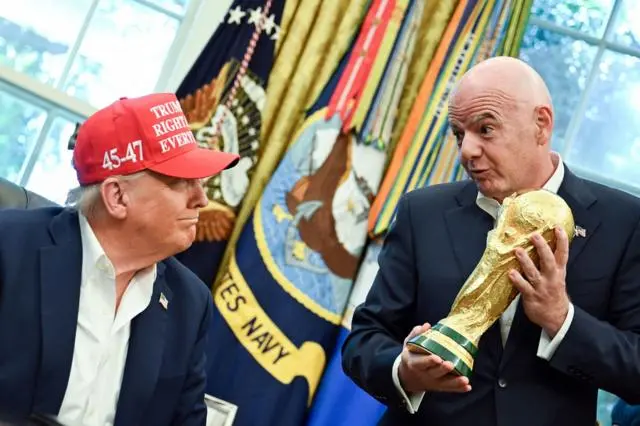 رئيس الاتحاد الدولي لكرة القدم (فيفا)، جياني إنفانتينو (إلى اليمين)، يسلم كأس العالم إلى الرئيس الأمريكي دونالد ترامب (إلى اليسار) بعد إعلانه عن إجراء قرعة كأس العالم 2026 في مركز كينيدي في ديسمبر/كانون الأول 2025.