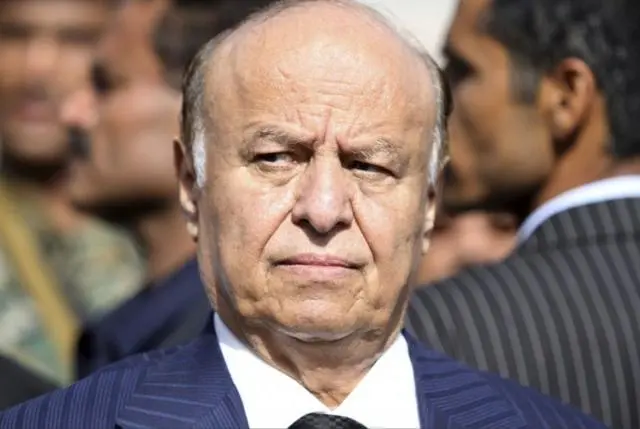 عبد ربه منصور هادي بين حشد مرتدياً لباساً رسمياً يميل إلى اللون الأزرق الغامق مع قميص أبيض.