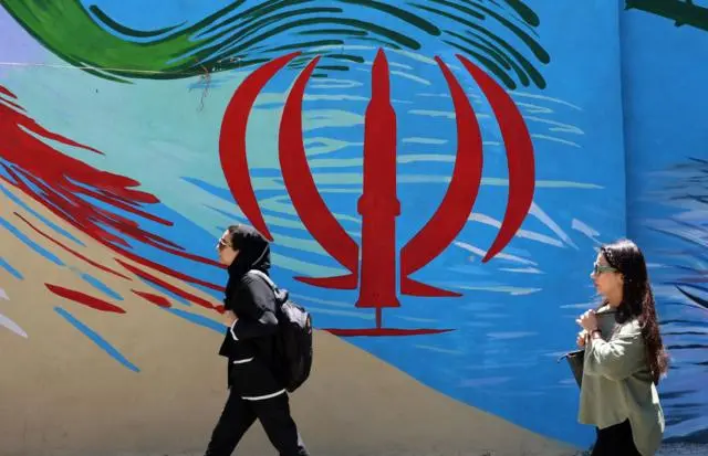 امرأتان إيرانيتان تمران أمام جدارية تحمل العلم الوطني الإيراني في أحد شوارع طهران.
