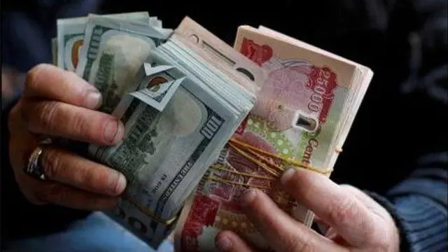 شخص يحمل بين كفيه دنانير عراقية ودولارات أمريكية.